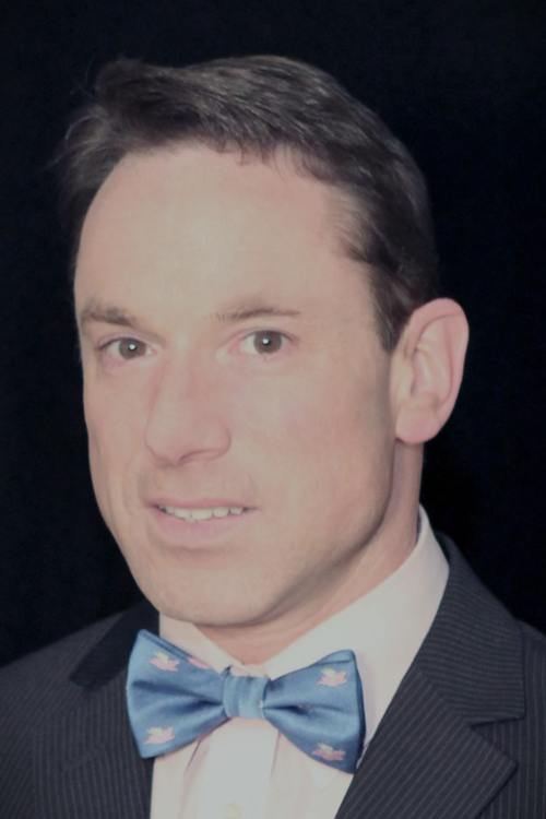 Man looking at camera, wearing a suit and light blue bowtie.