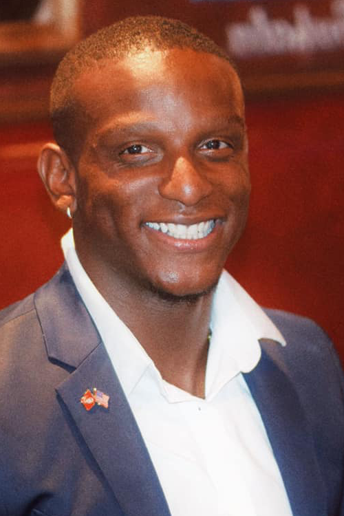 Man smiles and looks at camera, wearing a navy suit jacket and white shirt.